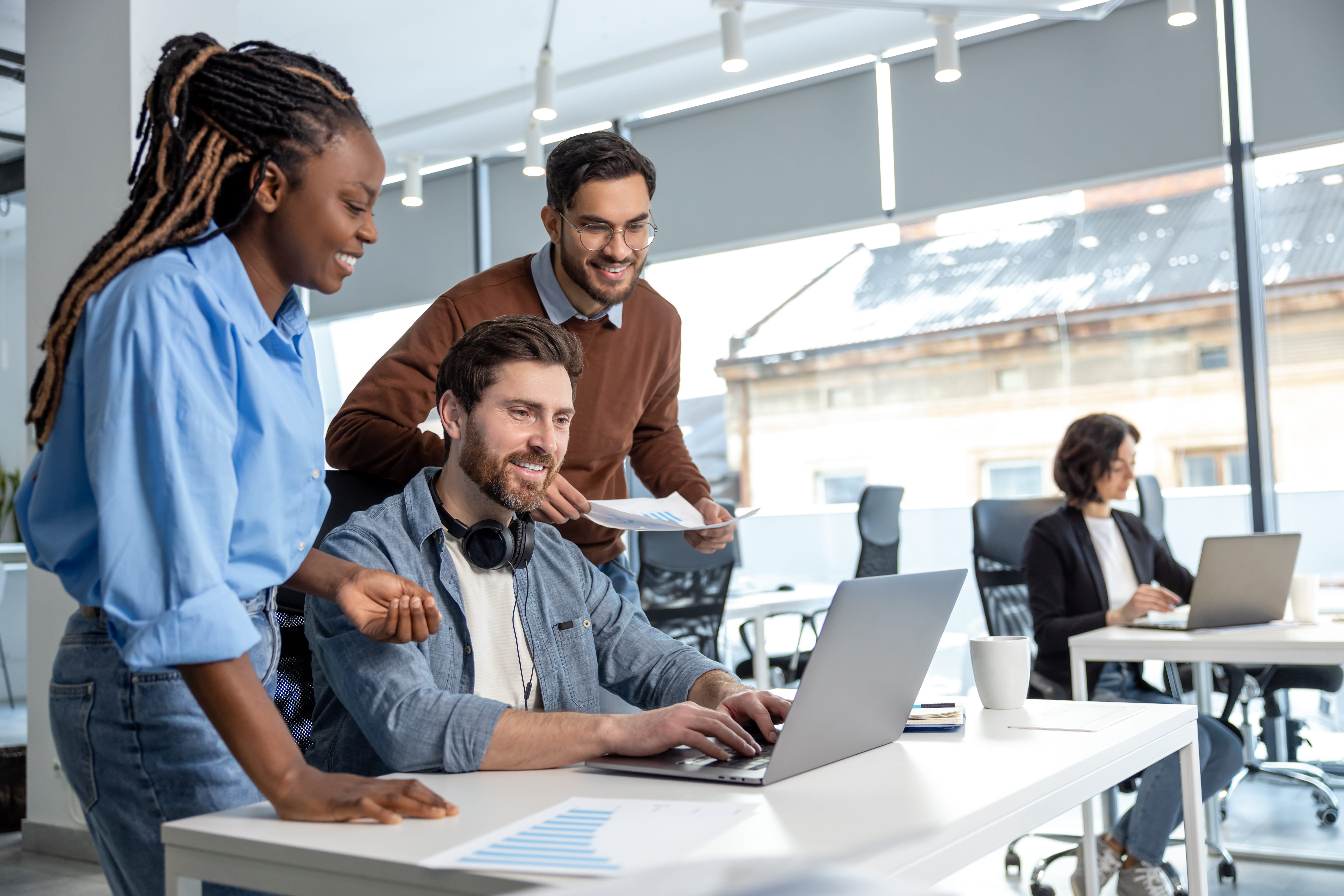 Three people in a modern office environment working together on a laptop, representing collaborative partnership